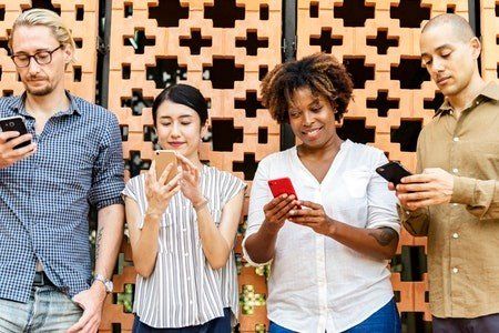 A group of people are standing next to each other looking at their phones.